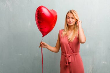 Eller, kızgın ve bazı ses işitme yorgun kulaklarıyla kapsayan zarif sarışın genç kadın portresi. Bir kırmızı kalp balon holding.