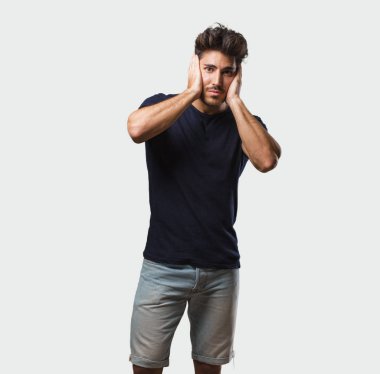 Genç yakışıklı adam ayakta eller, kızgın ve bazı ses işitme yorgun kulaklarıyla kaplama