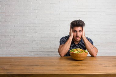 Eller, kızgın ve bazı ses işitme yorgun kulaklarıyla kapsayan bir masada oturan genç yakışıklı ve doğal adam. Taze bir salata yemek.