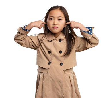 chinese little girl in beige trenchcoat covering her ears isolated on white background clipart