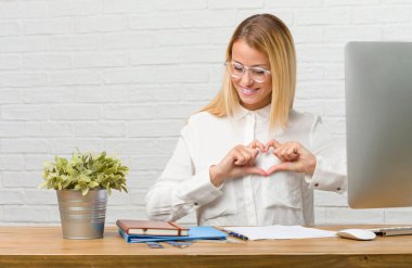 Sevgi ve dostluk, mutlu ve gülümseyerek kavramı ifade görevleri el ile bir kalp yapma yapmak masasına oturan genç bir öğrenci portresi