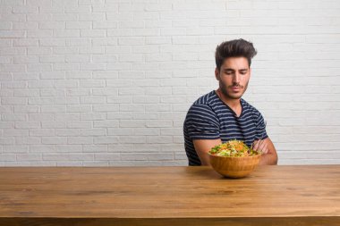 Kendinden emin ve göstermek güç hissi ve heybetli, kollarını, ciddi geçiş bir masada oturan genç yakışıklı ve doğal adam. Taze bir salata yemek.