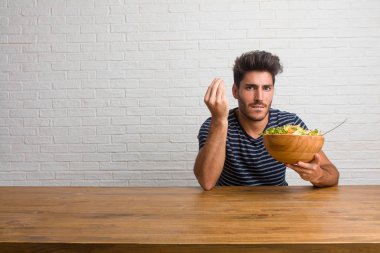 Tipik İtalyan jest, gülümseyen ve düz ileriye baktığımızda, simge veya el, çok doğal bir ifadeyle yapıyor bir masada oturan genç yakışıklı ve doğal adam. Taze bir salata yemek.