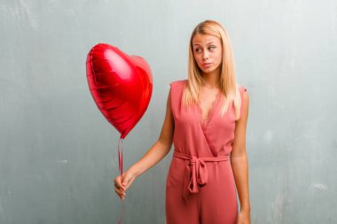 Portre sarışın genç zarif kadın şüphe ve karışık, düşünme, bir fikir ya da bir şey hakkında endişeli. Bir kırmızı kalp balon holding.