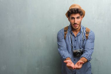 Hasır şapka, bir sırt çantası ve el ile bir şey tutan bir fotoğraf makinesi giyen genç yakışıklı gezgin adam bir ürün göstermek gülümseyen ve neşeli, hayali bir nesne sunan