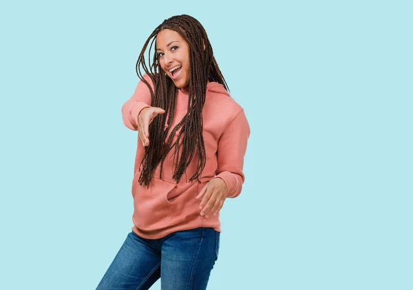 Portrait of a young black woman wearing braids reaching out to greet someone or gesturing to help, happy and excited