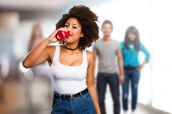 young black woman drinking soda drink with blurred people in background