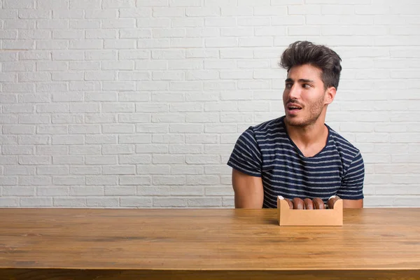 Young handsome and natural man sitting on a table very scared and afraid, desperate for something, cries of suffering and open eyes, concept of madness. Eating chocolate doughnuts.