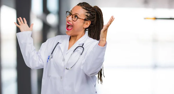 Portrait of a young black doctor woman screaming happy, surprised by an offer or a promotion, gaping, jumping and proud