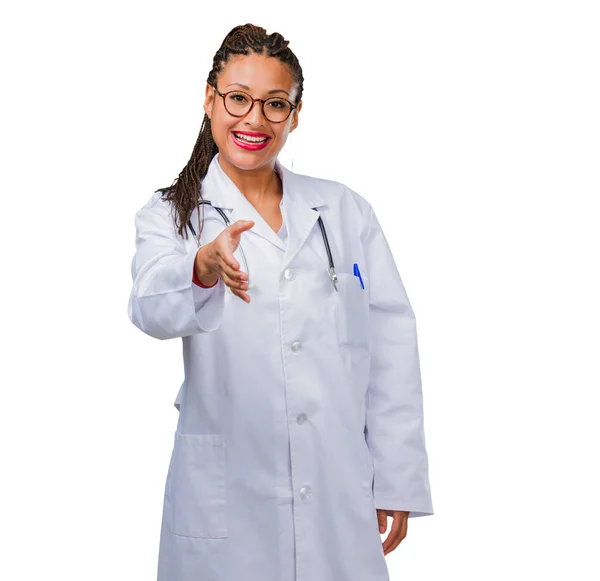 Portrait of a young black doctor woman reaching out to greet someone or gesturing to help, happy and excited