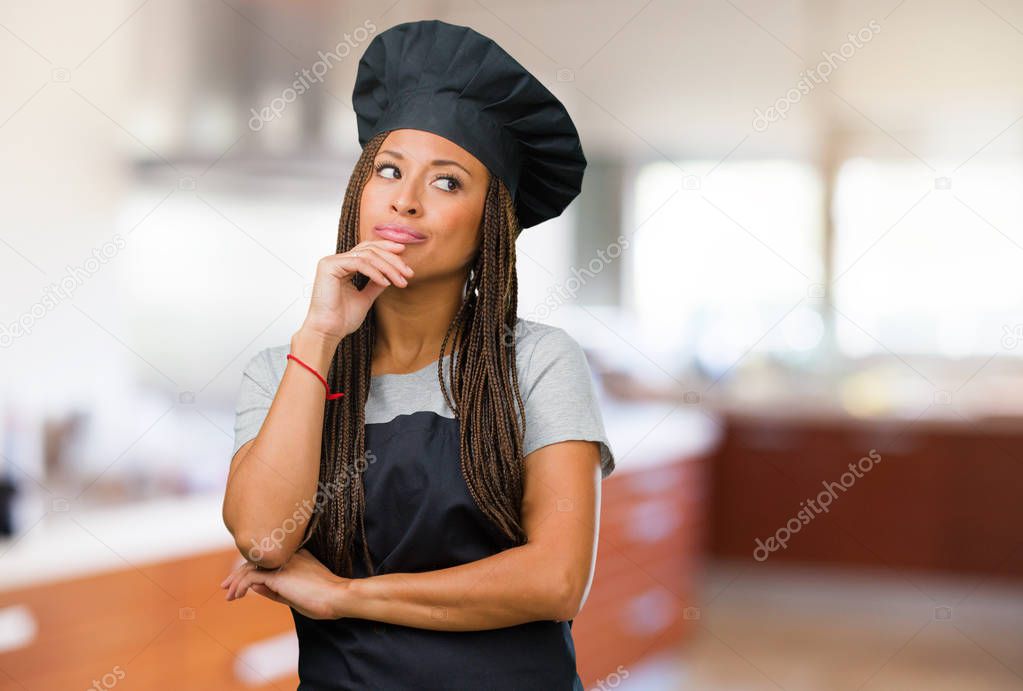 Portrait of a young black baker woman thinking and looking up, confused about an idea, would be trying to find a solution