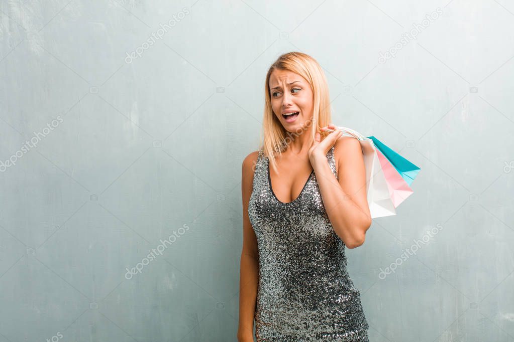 Portrait of young elegant blonde woman very scared and afraid, desperate for something, cries of suffering and open eyes, concept of madness. Holding shopping bag.