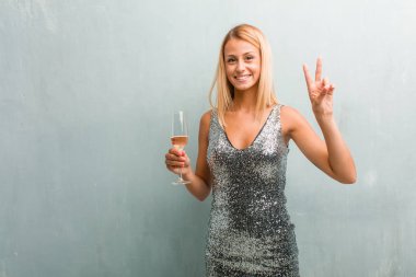 Gösterilen iki numaralı sayma simgesi, matematik, kendinden emin ve neşeli kavramı zarif sarışın genç kadın portresi. Bir şampanya kadehi holding.