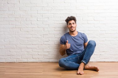 Doğal delikanlı oturup bir ahşap zemin üzerinde neşeli ve heyecanlı, gülümseyerek ve onu başparmak, başarı ve onay, ok jest kavramı yetiştirme