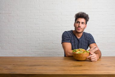Bir tablo şüphe ve karışık, düşünme, bir fikir ya da bir şey hakkında endişe üzerine oturan genç yakışıklı ve doğal adam. Taze bir salata yemek.