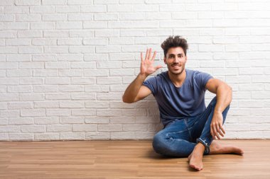 Doğal delikanlı oturup sayma, kavramı matematik, kendinden emin ve neşeli bir ahşap zemin gösteren sayı beş, sembolü