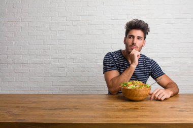 Bir tablo şüphe ve karışık, düşünme, bir fikir ya da bir şey hakkında endişe üzerine oturan genç yakışıklı ve doğal adam. Taze bir salata yemek.