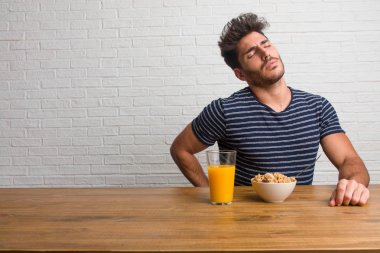 Sırt ağrısı nedeniyle iş stresi, yorgun ve zeki bir masada oturan genç yakışıklı ve doğal adam. Bir kahvaltı yapıyor, portakal suyu ve tahıl bowl içerir.