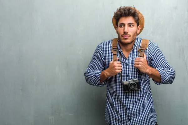 若いハンサムな旅人男麦わら帽子 バックパックと疑っている写真カメラを着て 肩をすくめて肩 優柔不断や不安 何か不安の概念 — ストック写真