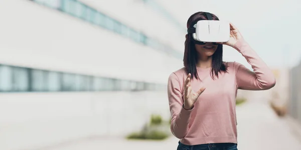 Young pretty woman excited and entertained, playing with virtual reality glasses, exploring a fantasy world, trying to touch something in the university campus