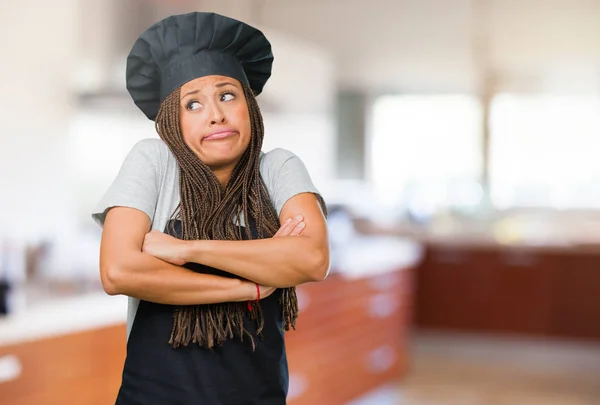 Portrait of a young black baker woman doubting and shrugging shoulders, concept of indecision and insecurity, uncertain about something