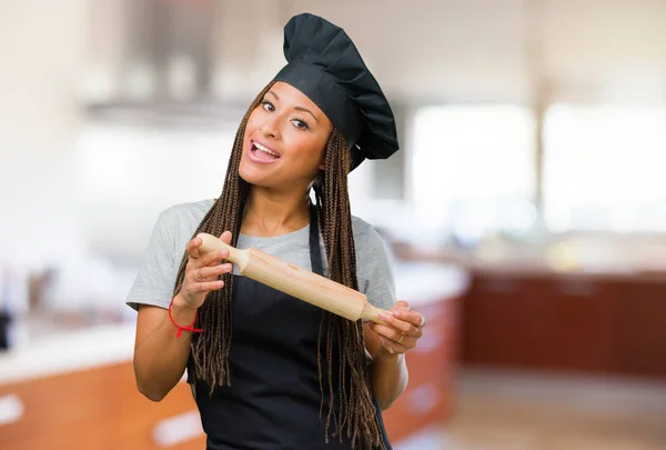 Portrait of a young black baker woman holding something with hands, showing a product, smiling and cheerful, offering an imaginary object