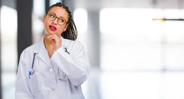 Portrait of a young black doctor woman thinking and looking up, confused about an idea, would be trying to find a solution