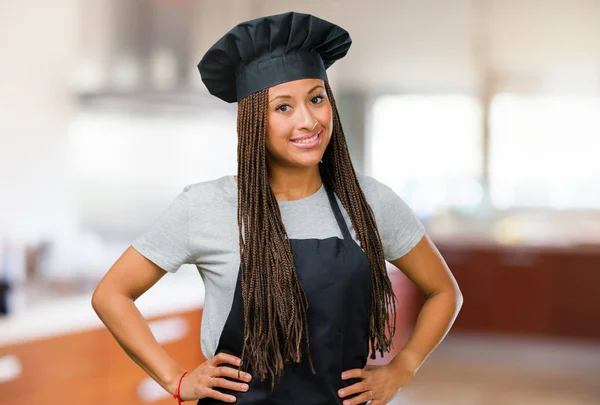 Portrait of a young black baker woman with hands on hips, standing, relaxed and smiling, very positive and cheerful