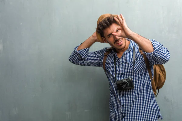 Young handsome traveler man wearing a straw hat, a backpack and a photo camera cheerful and confident doing ok gesture, excited and screaming, concept of approval and success