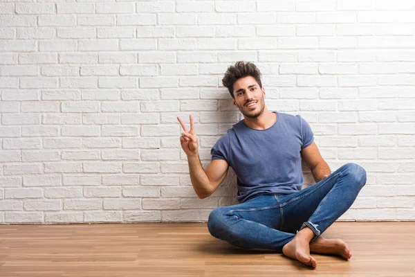 Young natural man sit on a wooden floor fun and happy, positive and natural, doing a gesture of victory, peace concept