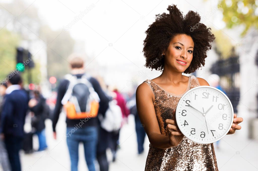 young black woman in stylish dress holding a big clock on blurred background