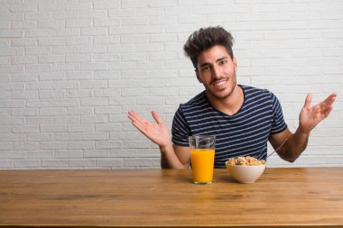Rahat ve neşeli, gülen ve having fun, bir masada oturan genç yakışıklı ve doğal adam kendinden emin ve başarılı hisseder. Bir kahvaltı yapıyor, portakal suyu ve tahıl bowl içerir.