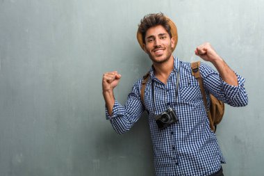 Silah, bir zafer ya da başarı, kutlama yükselterek bir hasır şapka, bir sırt çantası ve bir fotoğraf makinesi çok mutlu ve heyecanlı, genç yakışıklı gezgin adam Piyango kazanma