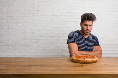 Öfkeli, negatif ve çılgın çığlık çok kızgın ve üzgün, çok gergin bir masada oturan genç yakışıklı ve doğal bir adam. Lezzetli bir pizza yemek.