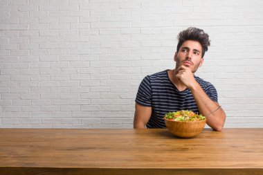 Bir tablo şüphe ve karışık, düşünme, bir fikir ya da bir şey hakkında endişe üzerine oturan genç yakışıklı ve doğal adam. Taze bir salata yemek.