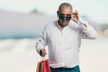 Orta yaşlı adam neşeli ve gülümseyen, alışveriş çantaları taşırken çok heyecanlı alışverişe gitmek ve yeni tekliflere bak hazır