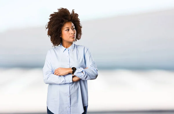 young black woman in blue shirt crossing arms on blurred background