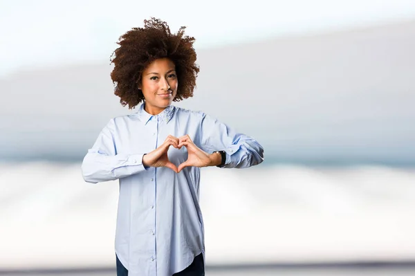 young black woman in blue shirt doing heart symbol on blurred background