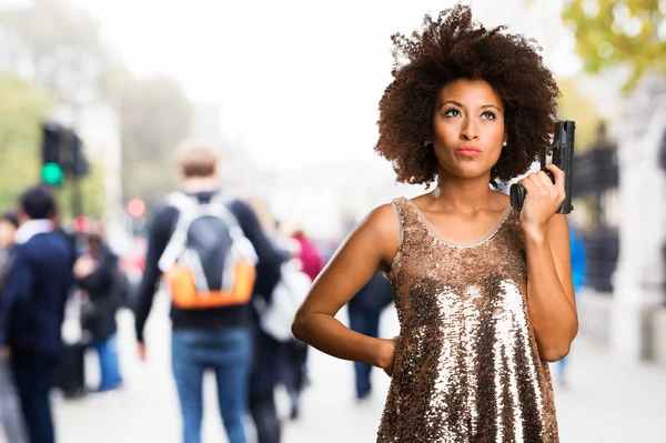 年轻的黑色妇女在时尚的礼服使用在模糊背景的枪 — 图库照片