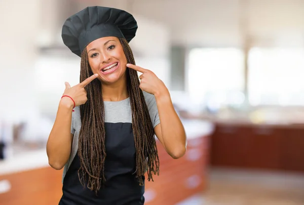 Portrait of a young black baker woman smiles, pointing mouth, concept of perfect teeth, white teeth, has a cheerful and jovial attitude