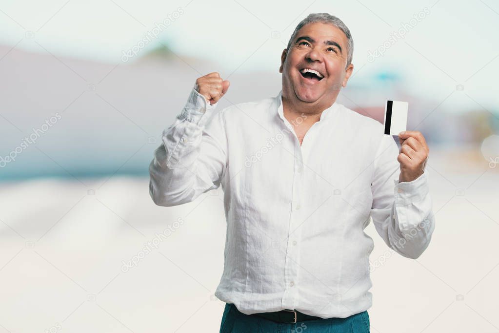 Middle aged man cheerful and smiling, very excited holding the new bank card, ready to go shopping