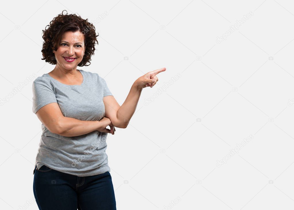 Middle aged woman pointing to the side, smiling surprised presenting something, natural and casual