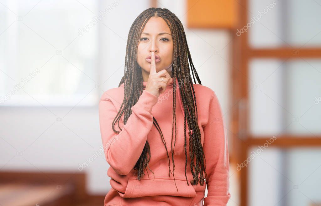 Portrait of a young black woman wearing braids keeping a secret or asking for silence, serious face, obedience concept