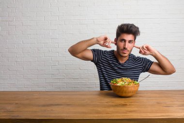 Eller, kızgın ve bazı ses işitme yorgun kulaklarıyla kapsayan bir masada oturan genç yakışıklı ve doğal adam. Taze bir salata yemek.