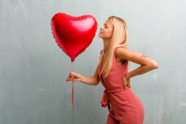 Sırt ağrısı nedeniyle iş stresi, yorgun ve zeki olan genç zarif sarışın kadın portresi. Bir kırmızı kalp balon holding.