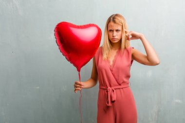 Bir konsantrasyon jest yapma zarif sarışın genç kadın adam portresi, seyir dümdüz bir hedef odaklı. Bir kırmızı kalp balon holding.