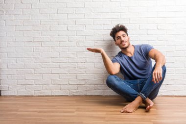 Doğal delikanlı oturup elleriyle bir şey tutan, bir ürün, gülümseyen ve neşeli gösterilen, hayali bir nesne sunan bir ahşap zemin üzerinde