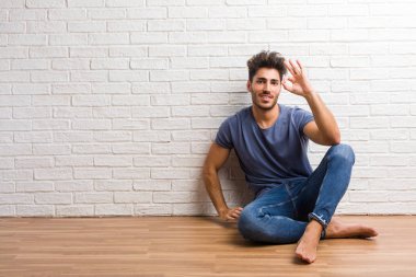 Doğal delikanlı oturup bir ahşap zemin üzerinde neşeli ve kendine güvenen heyecanlı ve çığlık, onay ve başarı kavramı ok jest yapıyor