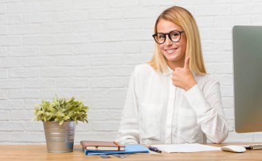 Genç öğrenci başarı ve onay, ok jest kavramı görevleri neşeli ve heyecanlı, gülümseyerek ve kadar parmağını yükselterek yapmak masasına oturan portresi