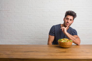 Bir tablo şüphe ve karışık, düşünme, bir fikir ya da bir şey hakkında endişe üzerine oturan genç yakışıklı ve doğal adam. Taze bir salata yemek.
